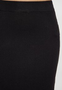 Nahaufnahme von schwarzem geripptem Strickstoff, der den elastischen Bund und die vertikalen Texturdetails zeigt.