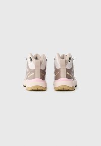 Beige and pink hiking shoes with a textured upper, padded collar, and rubber outsole. Features a pull tab and "Salomon" branding.