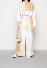 Pastelově zbarvený dvoudílný teplákový komplet s oversized topem a kalhotami s širokými nohavicemi. Obsahuje barevně rozlišený design v béžové, bílé a světlé hnědé barvě, s nastavitelným pasem.