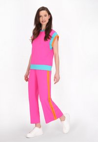 Roze sportoutfit bestaande uit een T-shirt met korte mouwen met turquoise en oranje accenten, gecombineerd met ruime broeken, aangevuld met witte sneakers.