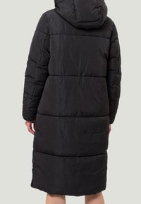 Abrigo acolchado negro con capucha, de longitud larga y textura acolchada con costuras horizontales. Bolsillos laterales con cremallera visibles.