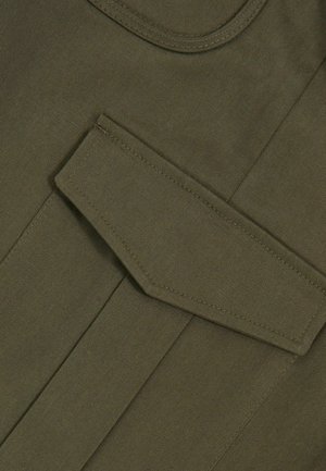 Olive rohelise tooni kangas, millel on sile tekstuur, sisaldab suurt, terava nurga jaotustaskut. Erinev õmblus servades rõhutab disaini.