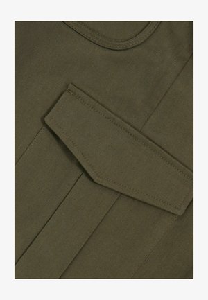 Olive rohelise tooni kangas, millel on sile tekstuur, sisaldab suurt, terava nurga jaotustaskut. Erinev õmblus servades rõhutab disaini.