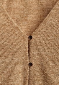 Beige gestrickte Strickjacke mit V-Ausschnitt, strukturierter Stoff und zwei dunkelbraunen Knöpfen vorne zum Schließen.