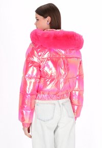 Różowa, opalizująca kurtka puchowa z kołnierzem z futerka ekologicznego, taliowana w pasie i z długimi rękawami. Stylizowana z jasnymi, dżinsowymi spodniami.