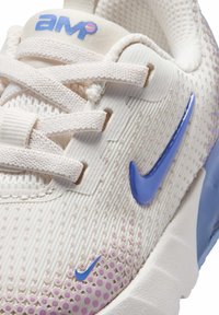 Κοντινό πλάνο του μπεζ αθλητικού παπουτσιού Nike Air Max Pulse με μπλε λογότυπο Swoosh και επάνω μέρος από διαπνέον υλικό με υφή.