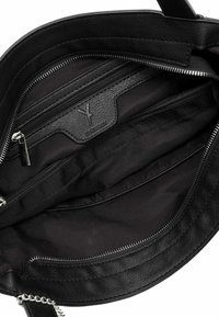 Intérieur d'un sac à main en cuir noir présentant plusieurs compartiments, y compris une poche zippée et un doublure en tissu lisse et foncé.