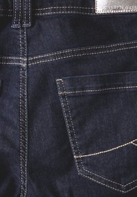 Jeans de mezclilla oscura con costuras visibles, un bolsillo trasero y una etiqueta de cuero. La tela tiene una textura suave con un ligero desvanecimiento.