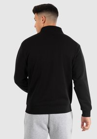 Zwarte pullover sweatshirt met hoge kraag en ribbelmanchetten, gemaakt van zacht materiaal, met een relaxte pasvorm en zonder zichtbare logo's.