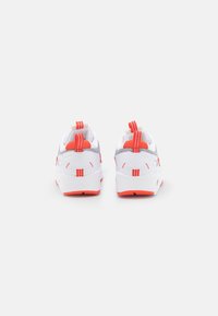Bílé sportovní boty s šedými akcenty a červenými úchyty. Obsahují texturované panely a polstrovanou podrážku, navržené pro pohodlí a podporu.