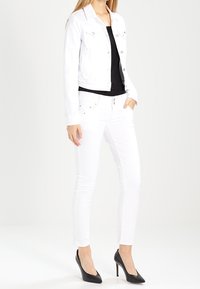 Valkoinen farkkutakki hopeisilla napeilla, yhdistetty mustaan toppiin ja valkoisiin skinny-farkkuihin. Mustat korkokengät täydentävät asun.