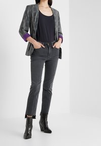 Blazer de cuadros grises con puños morados, camiseta sin mangas negra y jeans grises con dobladillo deshilachado. Combinado con botas negras de tobillo.