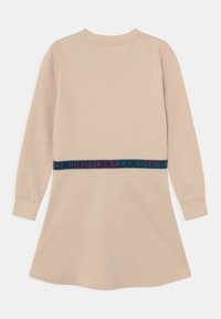 Beżowa sukienka z długim rękawem i rozkloszowanym dołem, z elastycznym paskiem w talii, ozdobiona wielokolorową taśmą z logo. Miękki, gładki materiał o minimalnej teksturze.