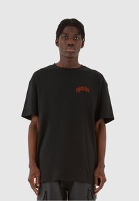 Svart bomull t-skjorte med avslappet passform og korte ermer. Har en liten oransje logo på brystet. Jevn tekstur, enkel design.