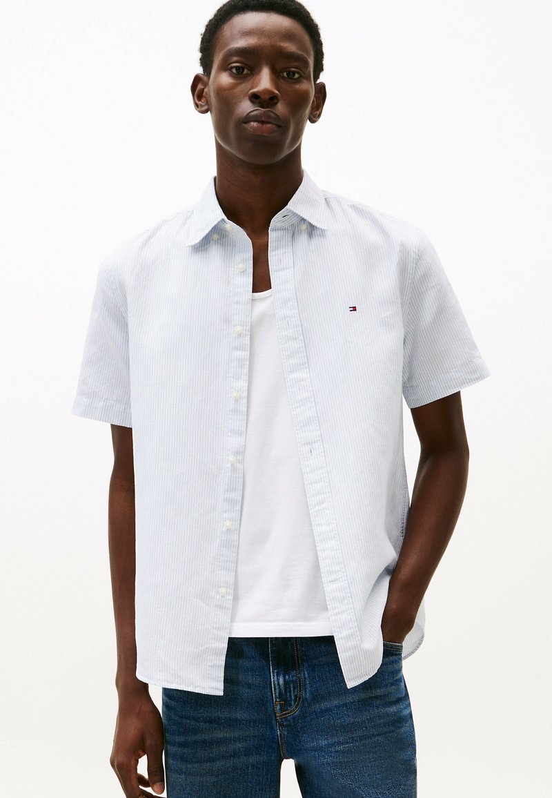 Camisa de manga corta de botones con rayas en azul claro y blanco, hecha de algodón, con un cuello puntiagudo y un pequeño logo en el pecho.