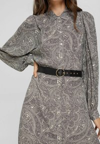 Robe à manches longues avec un motif paisley, dotée d'un col à revers et d'une ceinture noire à boucle circulaire, en tissu doux et texturé.