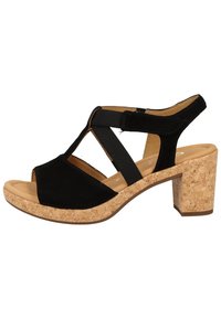 Sandale à talon en daim noir avec talon bloc en liège, design à bout ouvert et brides croisées élastiques pour un ajustement sûr. Doublure intérieure lisse couleur tan.