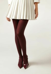 Bordowe rajstopy z gładkiej tkaniny, połączone z błyszczącymi bordowymi wysokimi obcasami, uzupełnione plisowaną białą spódnicą.