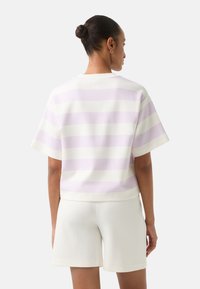 Krátký rukáv, cropped top z měkké tkaniny se střídajícími světlými fialovými a bílými pruhy; zakončeno kulatým výstřihem a volným střihem.