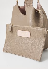 Beige leather handbag with textured finish, featuring a detachable pouch, gold hardware, and a pink accent label.