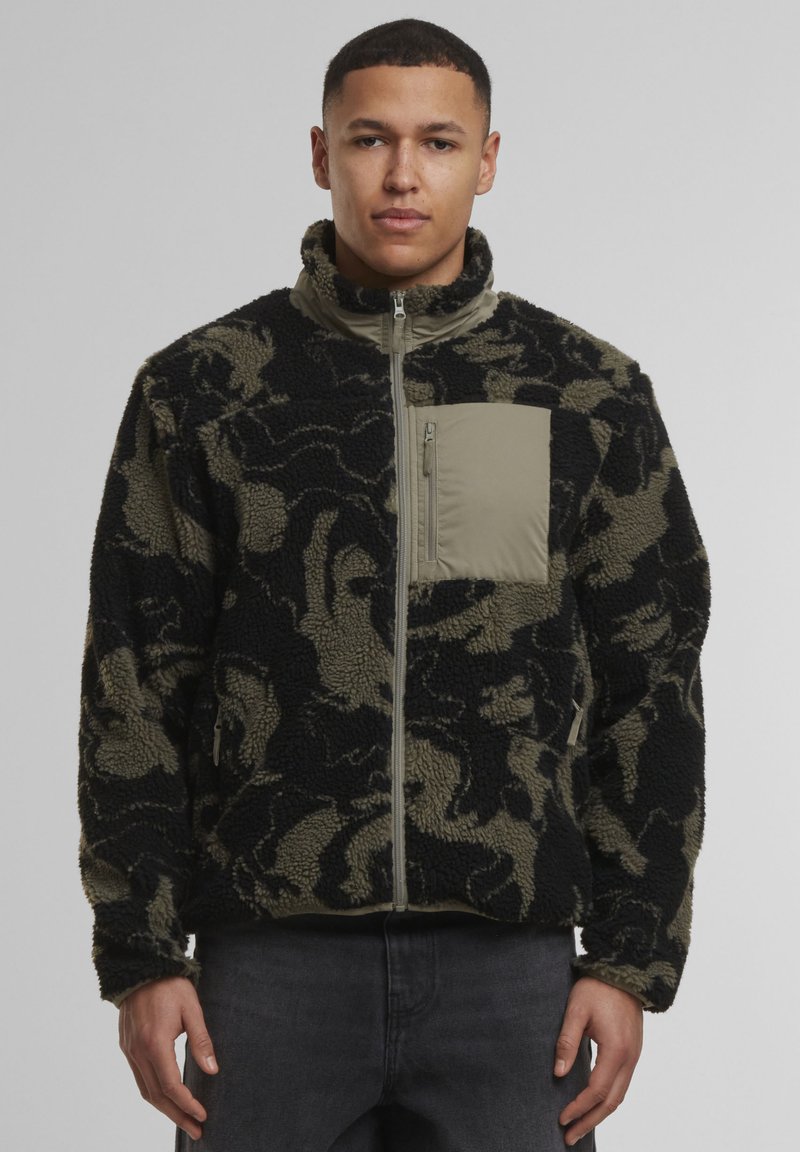 Fleecejacke mit schwarzem und olivgrünem Tarnmuster, hohem Kragen, durchgehendem Reißverschluss und einer kontrastierenden Brusttasche in solidem Olivgrün.