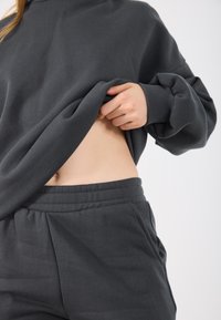 Sudadera gris oscuro y pantalones de chándal a juego con un ajuste relajado. Tela suave, con puños acanalados y cinturilla elástica.