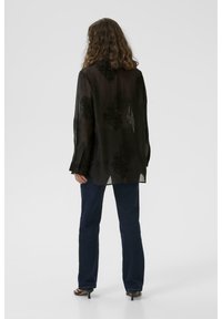 Black sheer blouse with floral pattern, long sleeves, and button cuffs, paired with dark blue straight-leg jeans and black heeled sandals.