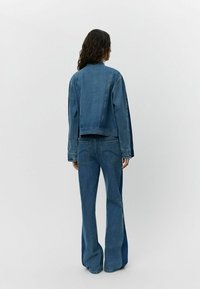 Set di giacca in denim e jeans svasati in blu medio. Presenta una giacca corta con taglio dritto e tasche sul retro dei jeans.