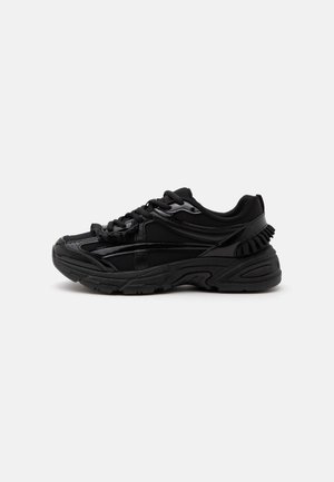 Baskets de sport noires avec des détails en mesh et brillants, semelle épaisse et rembourrée, fermeture à lacets, vue de profil sur fond blanc.