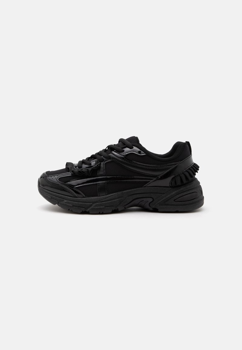 Baskets de sport noires avec des détails en mesh et brillants, semelle épaisse et rembourrée, fermeture à lacets, vue de profil sur fond blanc.