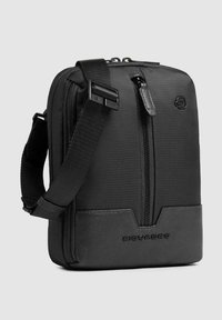 Zwarte boodschapperstas met een gestructureerde stof en een glad leren bodem, voorzien van een ritssluiting en een verstelbare riem.