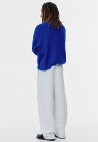 Oversized blauwe trui met een getextureerde brei, gecombineerd met lichtgrijze, brede broekspijpen. Zwarte schoenen maken de outfit compleet.