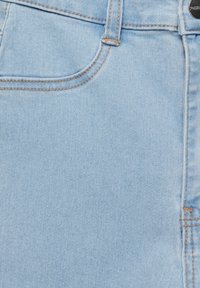 Tissu en denim bleu clair avec poche avant visible, surpiqûres orange, passants pour ceinture et bouton métallique sur le jean.