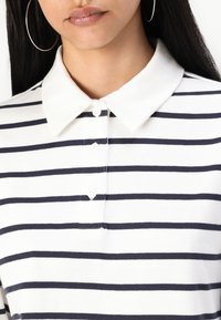 Collared polo shirt featuring white fabric with navy horizontal stripes, five-button placket, and smooth texture.