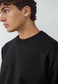 Czarny sweter z okrągłym dekoltem i ribbowanym wykończeniem. Miękka tekstura, swobodny fason i dopasowane rękawy. Brak widocznych grafik lub wzorów.