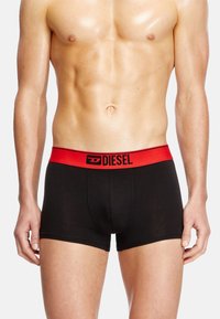 Caleçons boxers noirs avec une large taille élastique rouge portant l'inscription "DIESEL" en noir. Le tissu semble lisse et bien ajusté contre la peau.