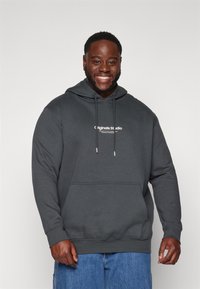 Sudadera gris oscura hecha de tela suave. Presenta cordones, un bolsillo frontal y texto del logo de la marca en blanco en el pecho. Corte informal.