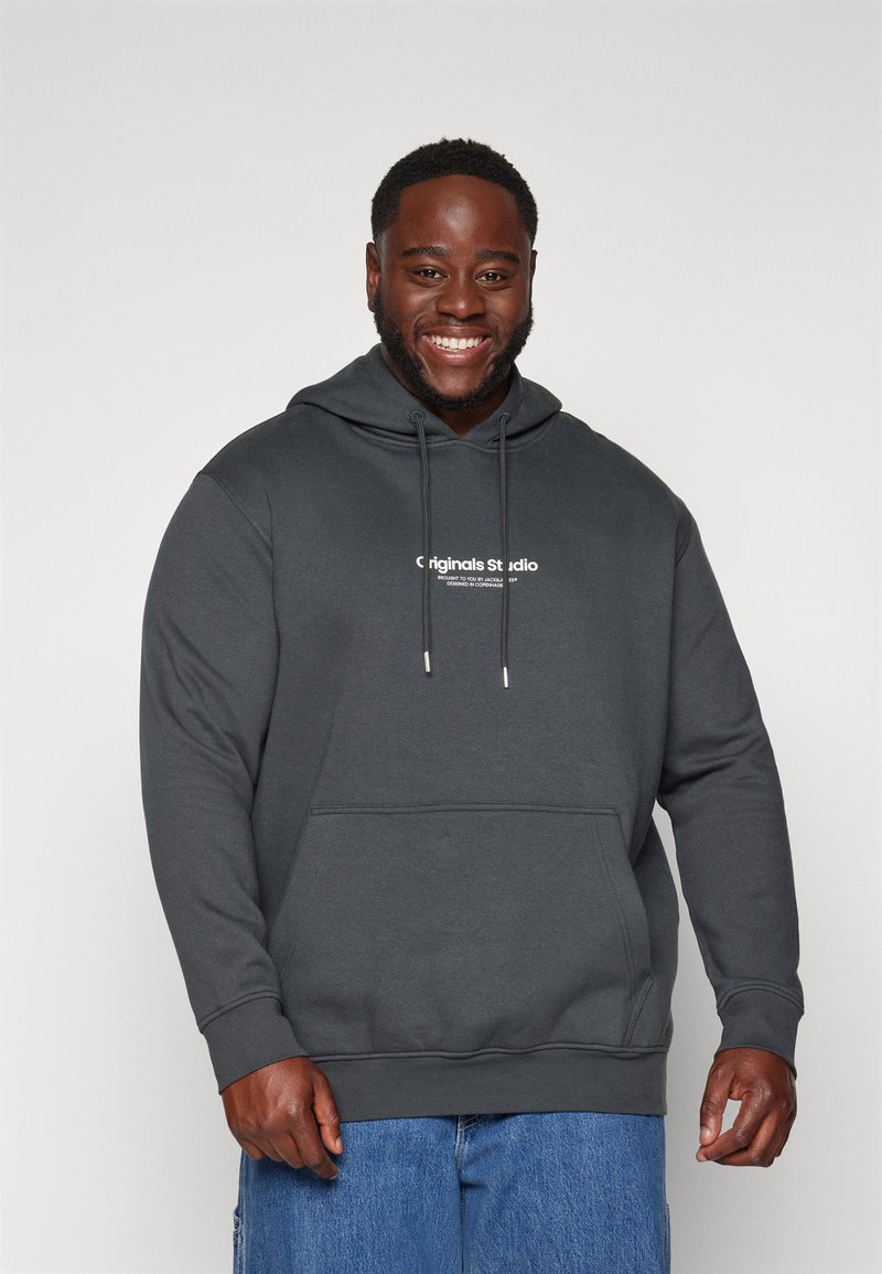 Sudadera gris oscura hecha de tela suave. Presenta cordones, un bolsillo frontal y texto del logo de la marca en blanco en el pecho. Corte informal.
