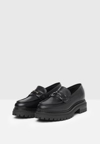 Mocassins en cuir noir avec une semelle plateforme épaisse, ornés d'une boucle métallique décorative et d'une finition lisse.