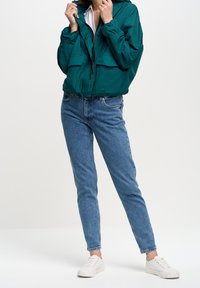 Jasnoniebieska, lekka kurtka z regulowanym kapturem, dwoma przednimi kieszeniami, zestawiona z jasnoniebieskimi dżinsami i białymi trampkami z nakrapianą podeszwą.