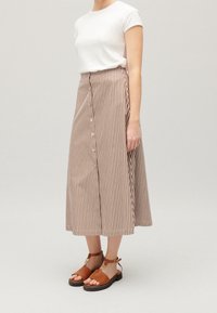 Brun- och vitrandig midikjol med knappar framtill. Kombinerad med bruna sandaler och en figurnära vit t-shirt.