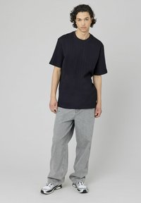 T-shirt noir à manches courtes côtelé avec un col rond, associé à un jean large gris clair et des chaussures de sport noir et blanc.