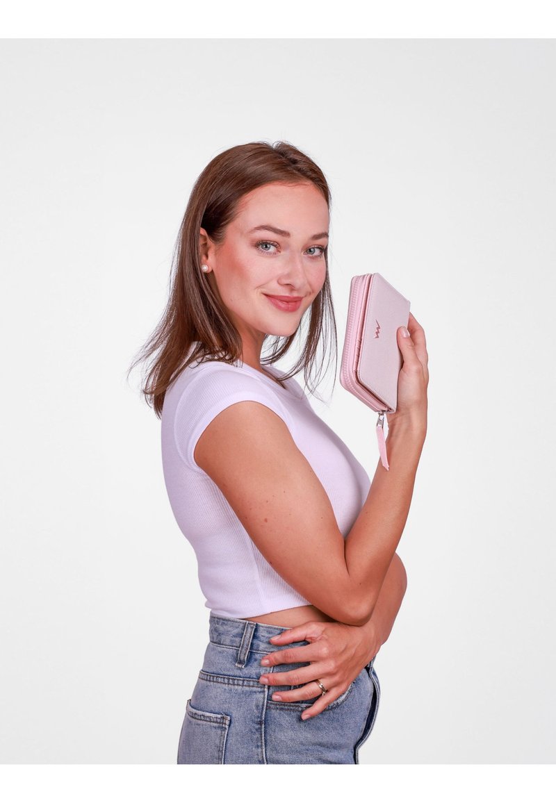 Light pink zippered wallet with textured finish, featuring a wrist strap and embossed brand logo, held by a person wearing a white top.