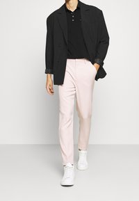 Svart dubbelknäppt blazer, svart polo, ljusrosa byxor och vita sneakers. Har släta texturer och skräddarsydd passform.