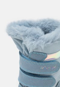 Blå snøstøvler med mykt faux fur-pynt, stoffoverdel, borrelåsremmer og en skinnende iriserende aksent. Strukturert detalj langs remmenes kanter.