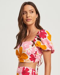 Top corto floreale rosa con maniche a sbuffo corte, scollatura quadrata e dettaglio con fiocco sul retro; motivi di fiori gialli e rossi vivaci.