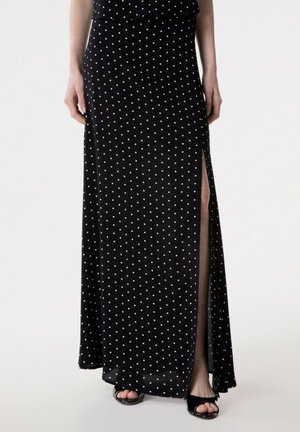 Gonna lunga nera con pois bianchi e spacco laterale, indossata con tacchi neri open-toe.