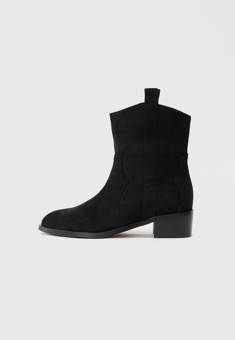 Botine negre din suede, cu vârful rotunjit, cusături curbe și un toc bloc mic. Prezintă un tab pentru a fi purtate ușor.