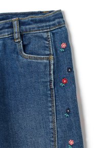 Vaqueros de mezclilla con tejido azul, que presentan bordados florales en rosa, rojo y marino a lo largo del costado, diseño de cinco bolsillos y costuras en contraste.