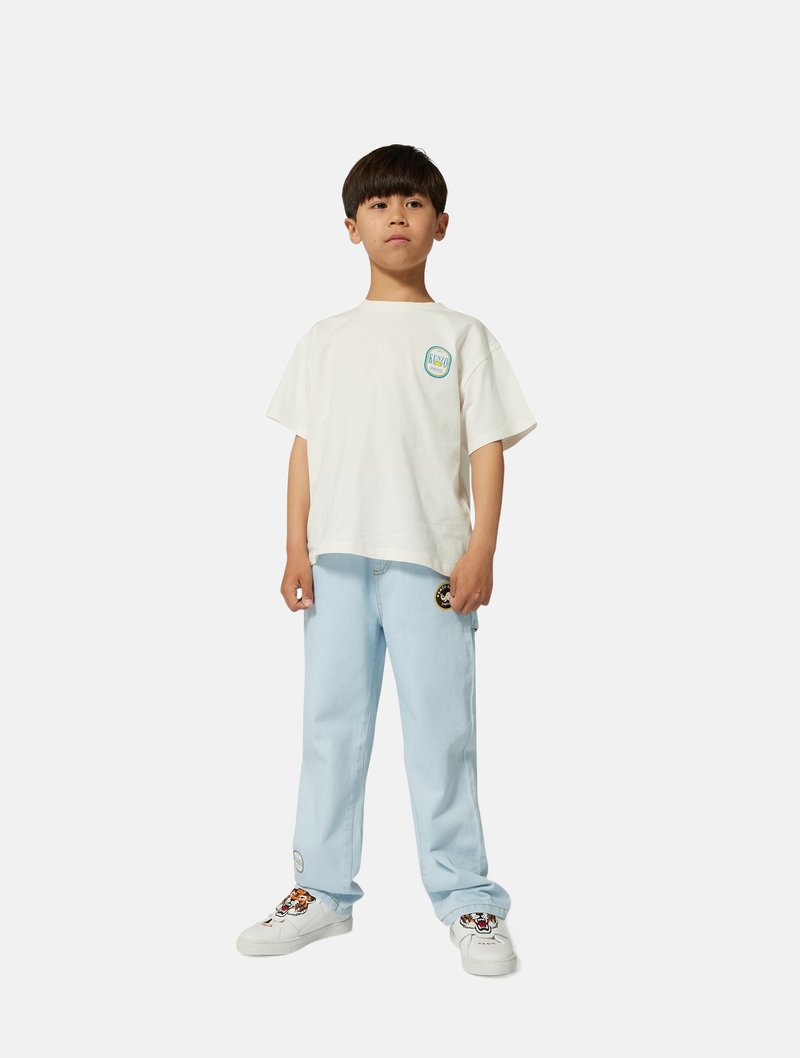 Witte t-shirt met korte mouwen met een ronde patch, lichtblauwe jeans en witte sneakers met een kleurrijk tijgerontwerp en ronde patches.